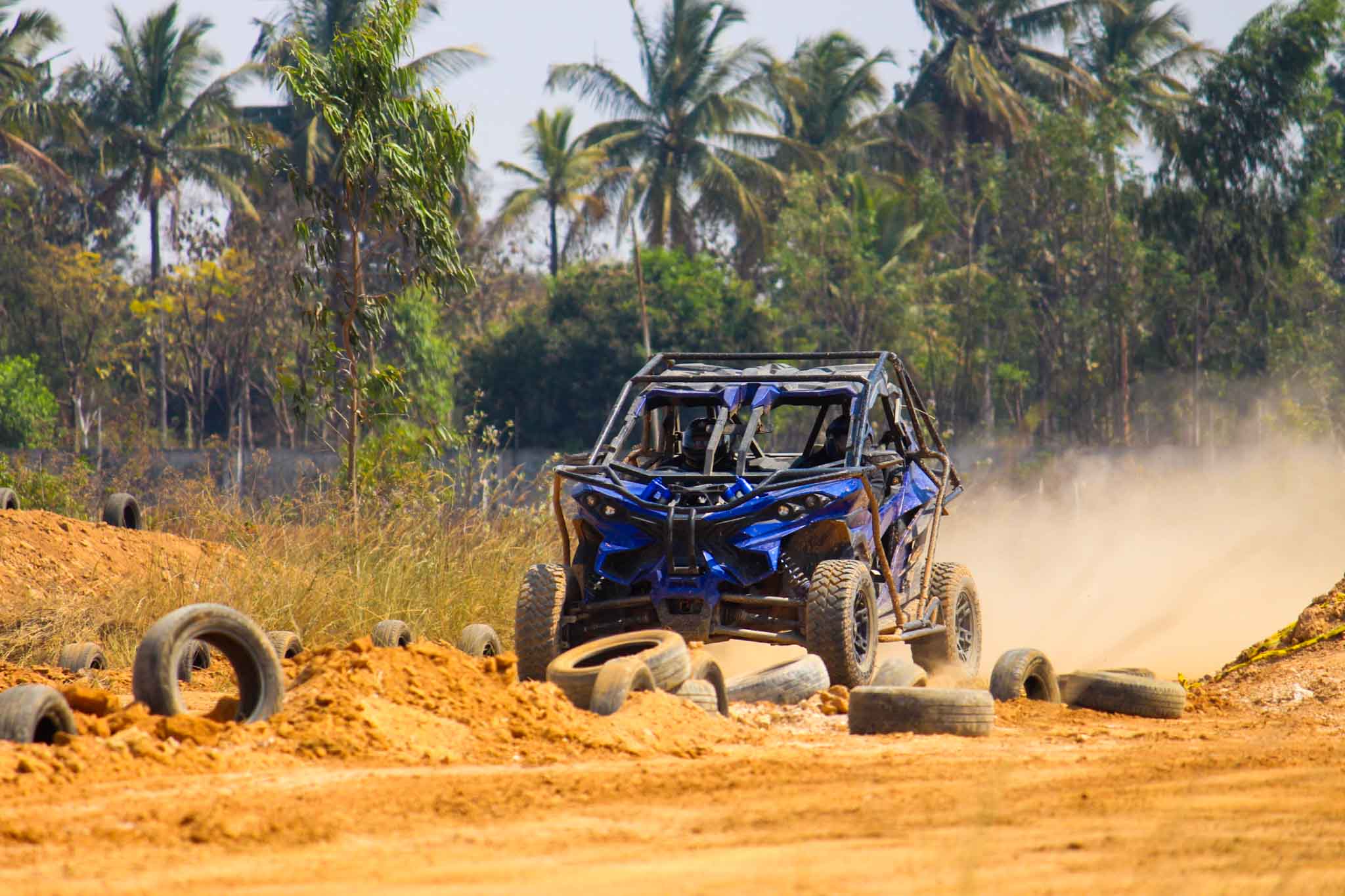 Blue off-road ATV driving aggressively on dirt track surrounded by tires and trees.